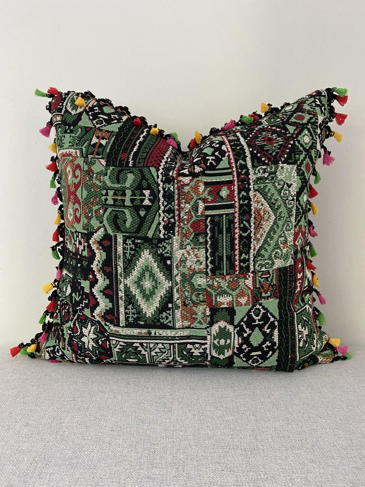 Green boho patchwork cushion cover 50x50 cm with multicolour tassel trim, front view on a grey sofa