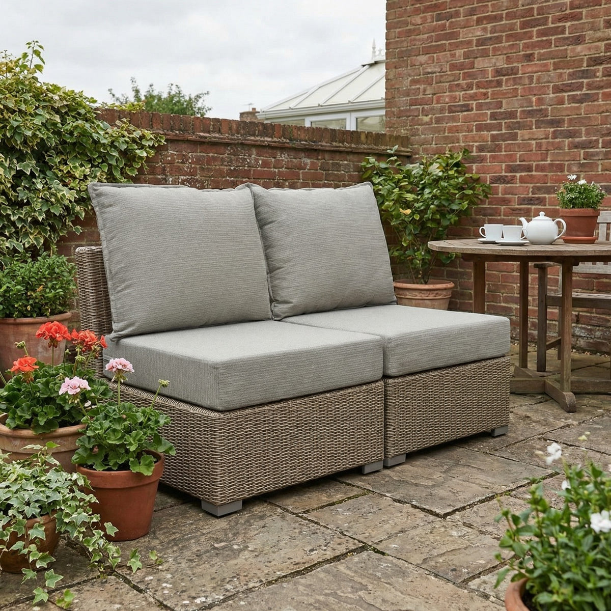 Two neutral grey outdoor cushion sets on rattan modular chairs on a brick-walled patio