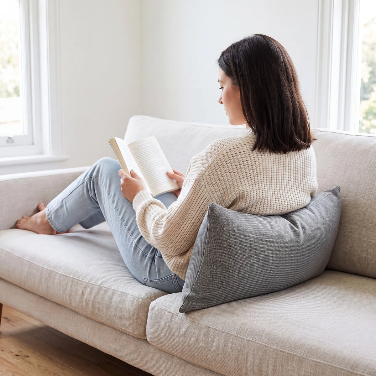 Grey lumbar cushion giving lower back support to a woman reading on a cream sofa