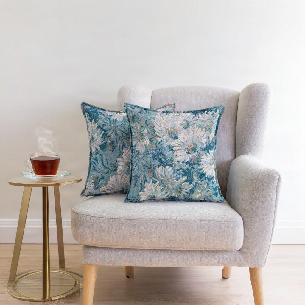 Pair of teal daisy tapestry cushion covers on a cream wing armchair beside a gold side table