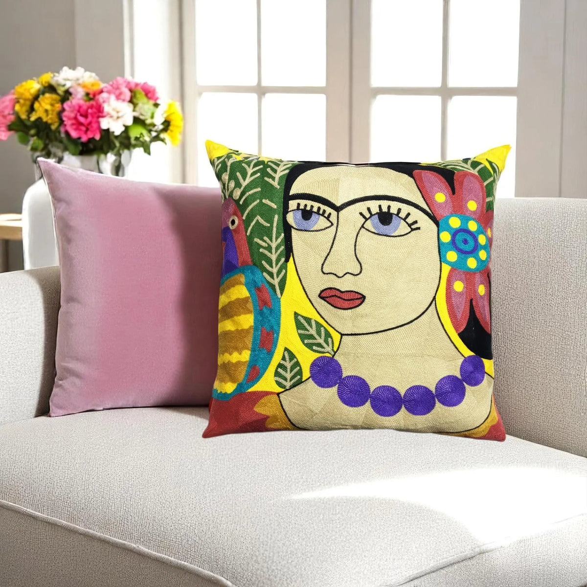 Boho embroidered cushion cover with a parrot and leaves on a light grey sofa beside a pink cushion