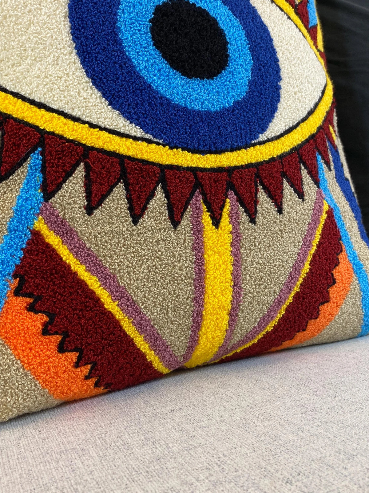 Detail of the tufted zigzag stripes in burgundy, orange, yellow and mauve on the cushion cover