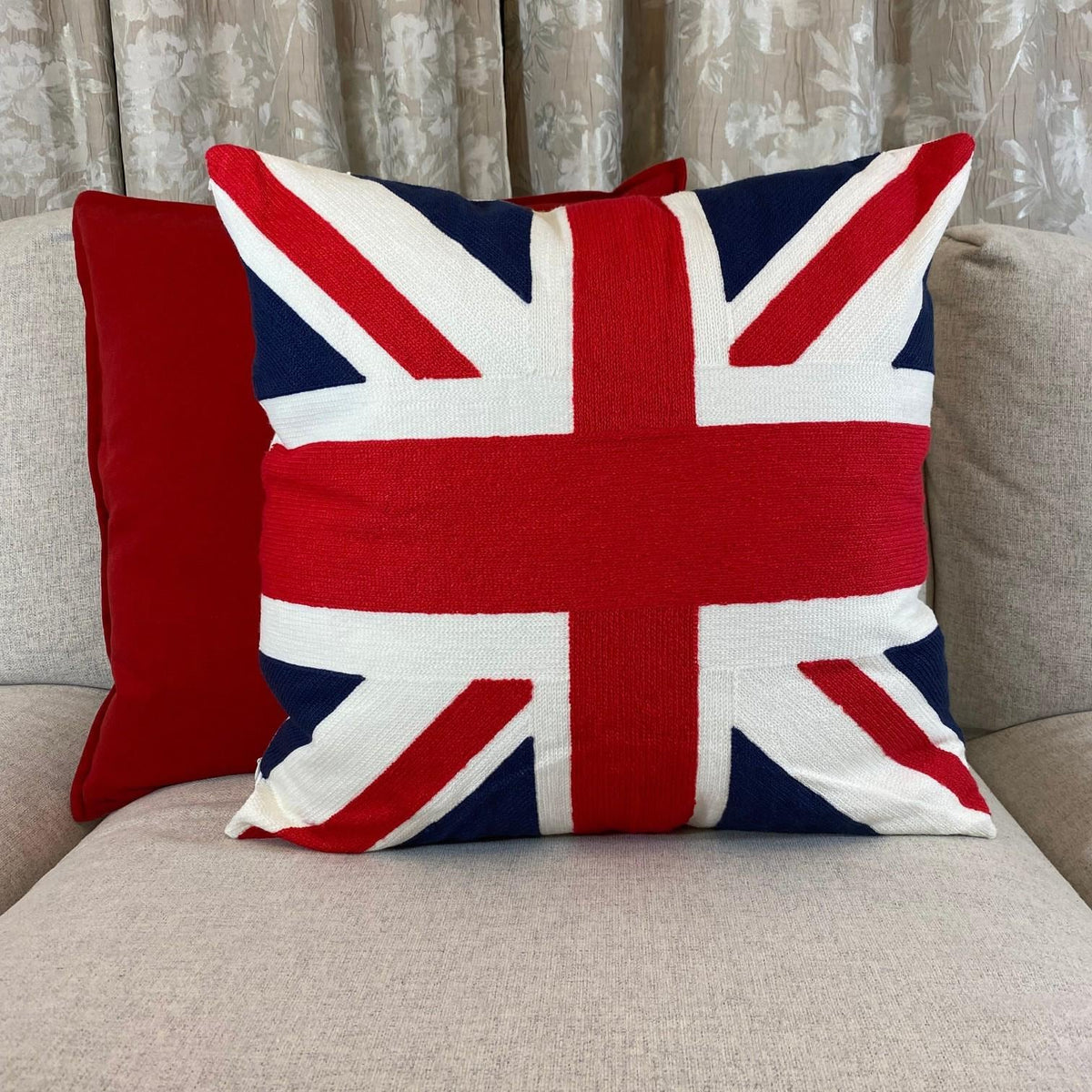 Embroidered Union Jack cushion on a light grey sofa beside a plain red cushion