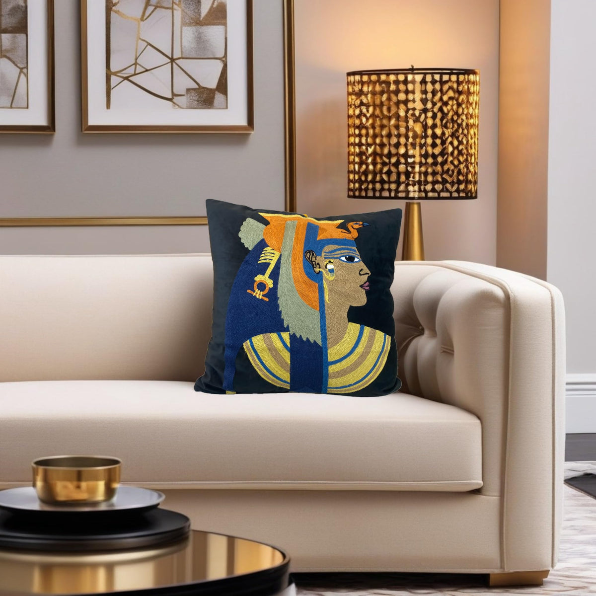Egyptian Cleopatra cushion cover on a cream sofa beneath a gold lamp and framed art