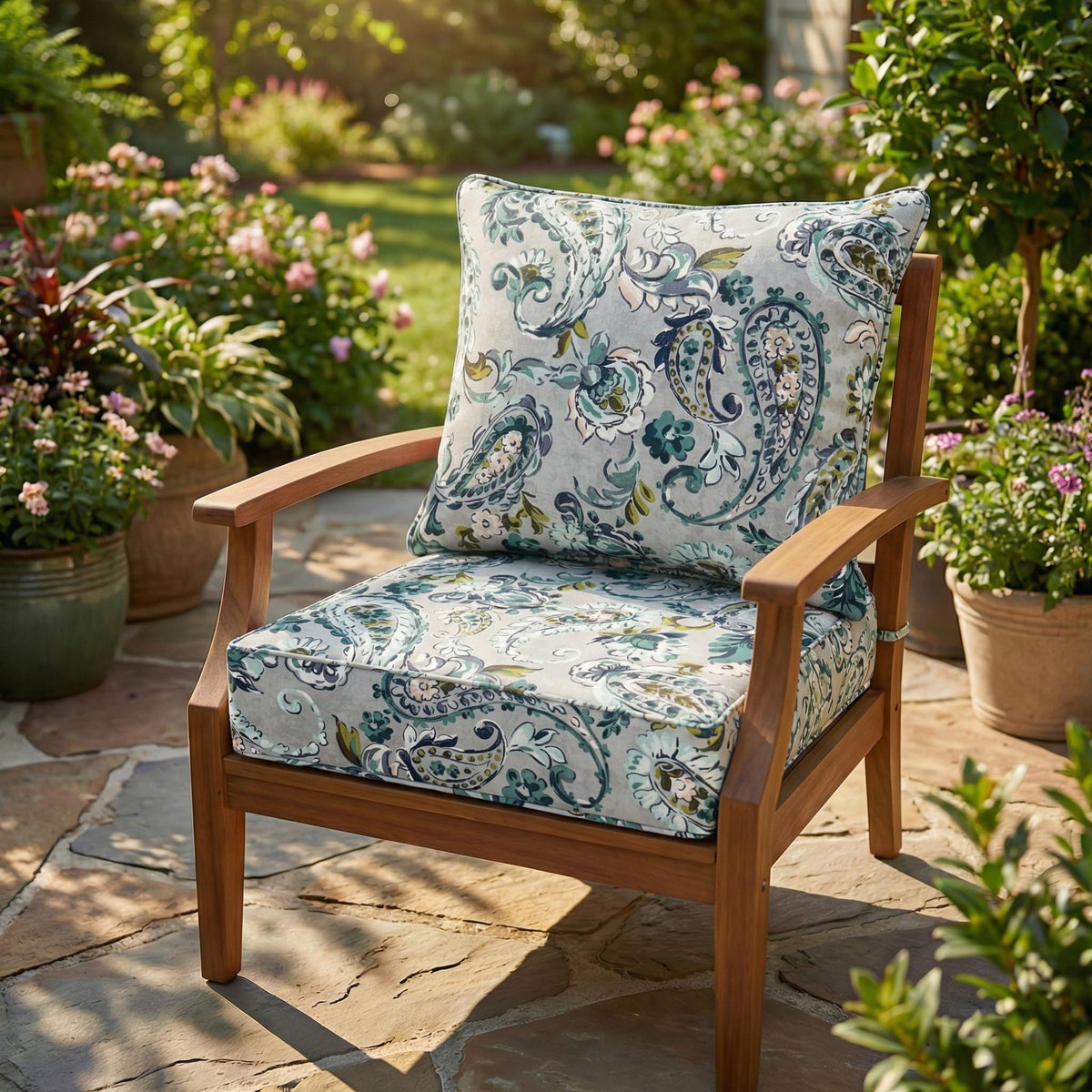 Grey and teal paisley garden cushions on a teak armchair on a sunny stone patio