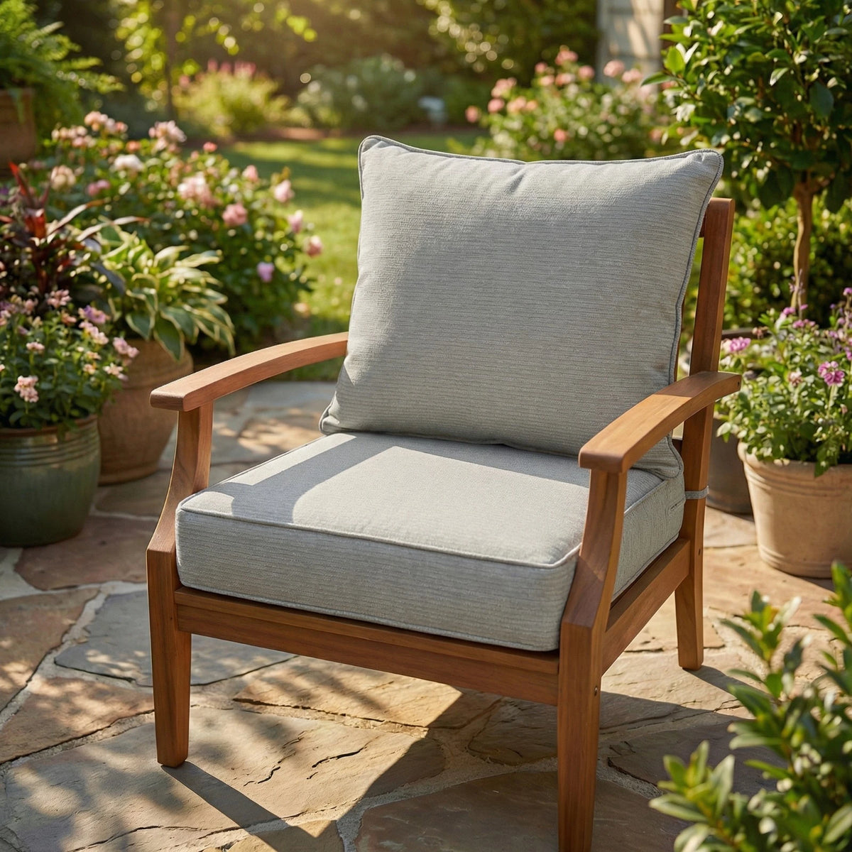 Neutral grey outdoor cushion set on a teak garden armchair, plain textured seat and back cushions