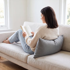 Grey lumbar cushion giving lower back support to a woman reading on a cream sofa