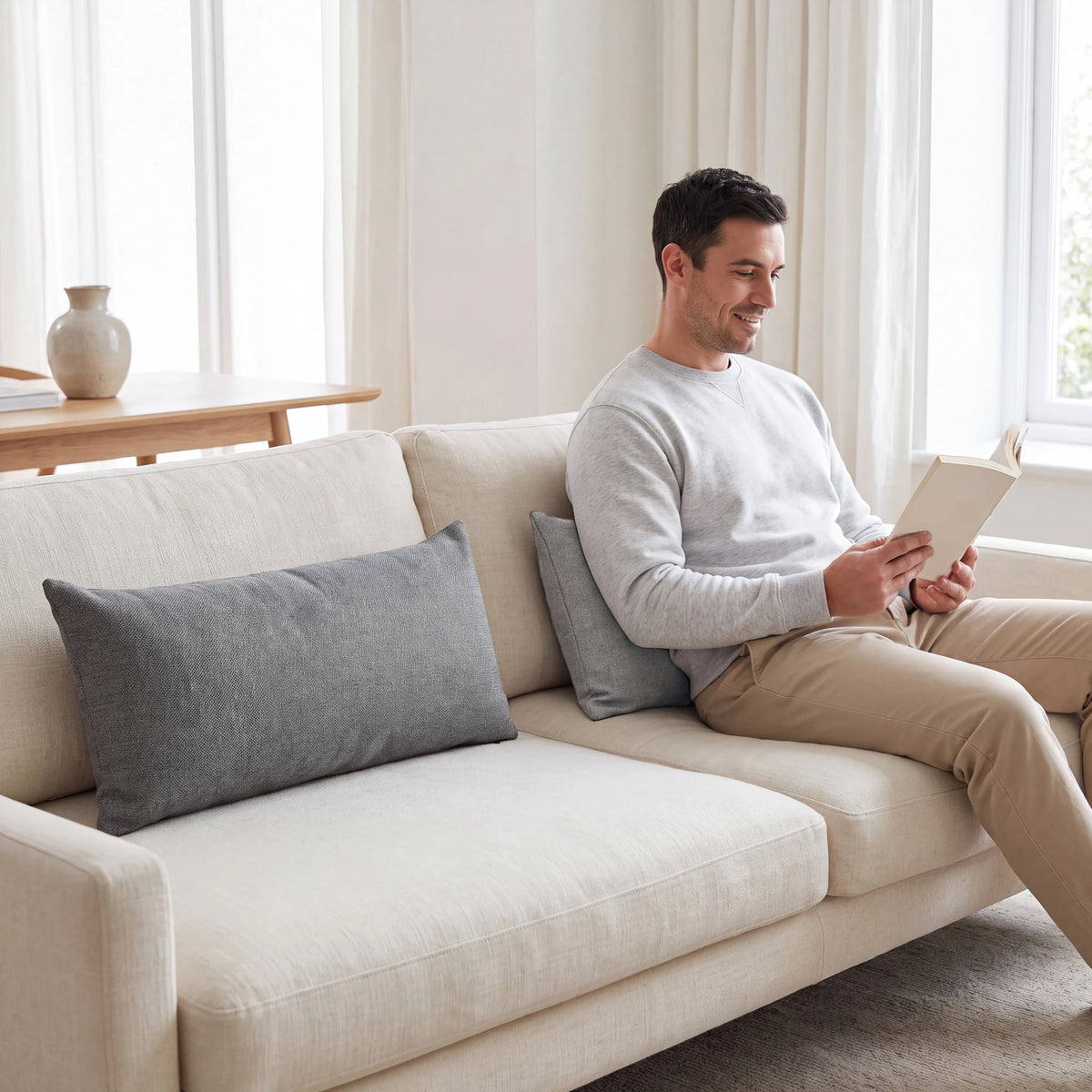 Two grey lumbar cushions styling a cream sofa, one behind a man reading a book