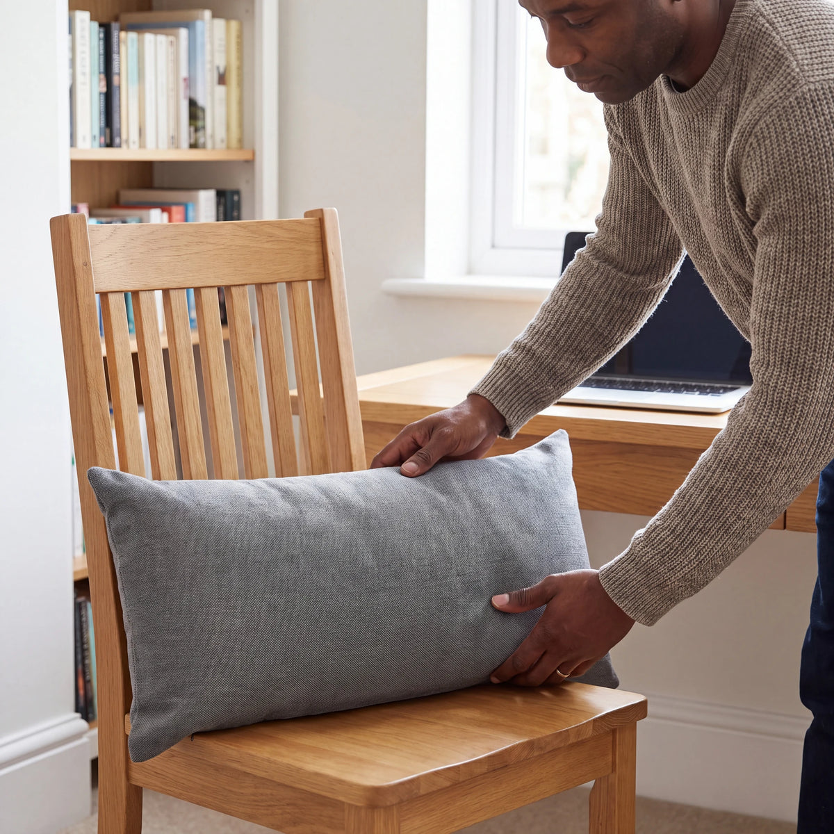 Grey back support cushion being placed on a wooden desk chair in a home office