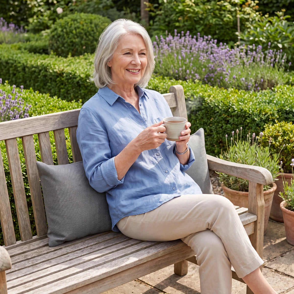 Grey outdoor lumbar cushions on a garden bench behind a woman holding a cup of tea