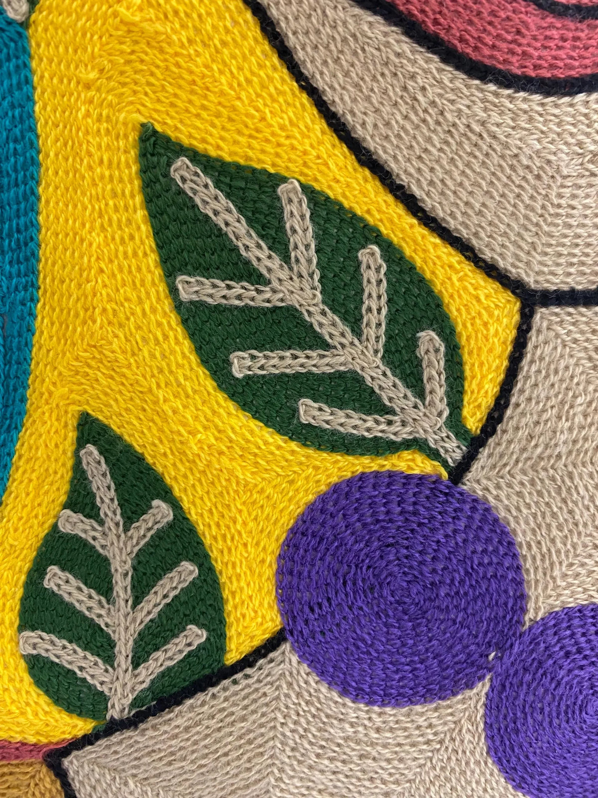Detail of the embroidered cushion cover front: yellow ground, green leaves and purple bead necklace