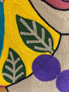 Detail of the embroidered cushion cover front: yellow ground, green leaves and purple bead necklace