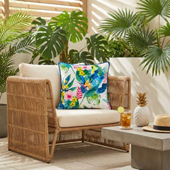 Ivory floral velvet cushion cover on a wide rattan armchair among palms and monstera