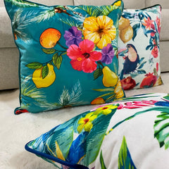 Teal tropical, toucan and floral velvet cushion covers layered on a cream sofa and sheepskin rug