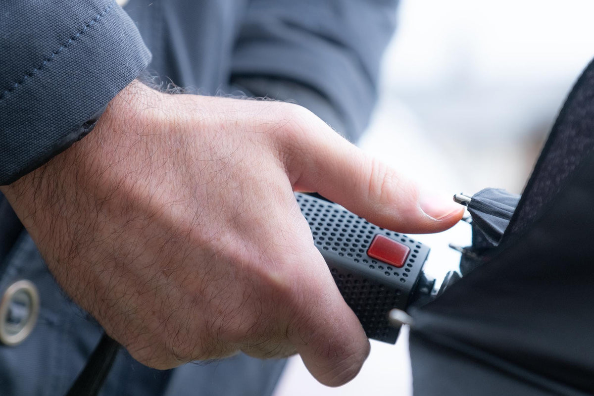 Hand pressing the red button that opens and closes the automatic compact umbrella