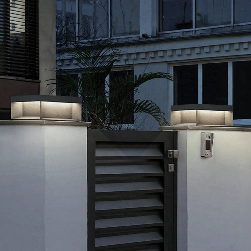 Pair of square gate post lights glowing on rendered pillars either side of a garden gate