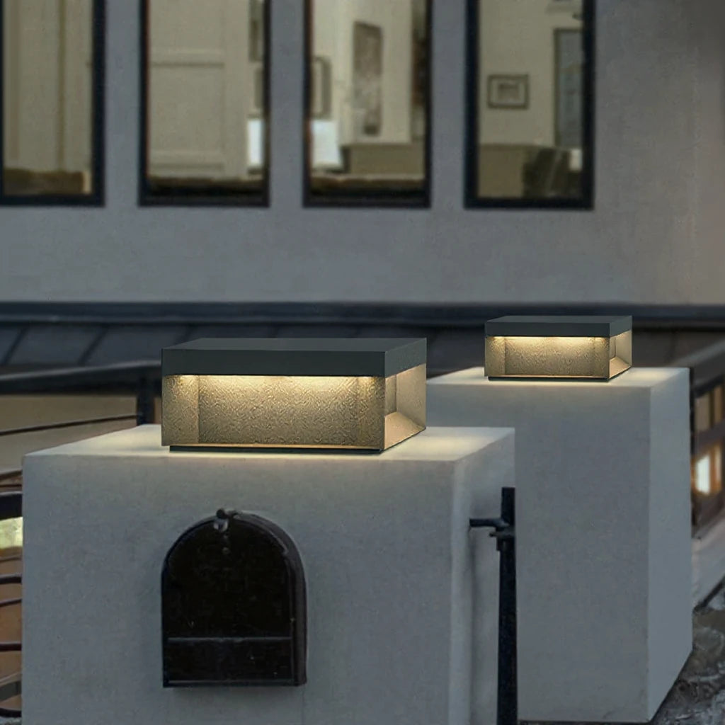 Square pillar cap lamps lit on two white rendered gate piers outside a house at dusk