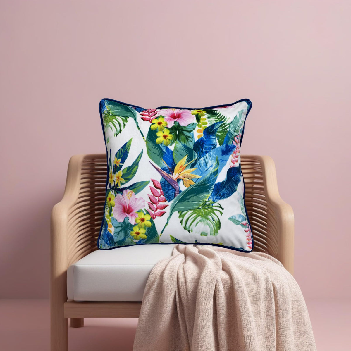 Ivory floral cushion cover on a rattan chair against a blush pink wall with a knitted throw