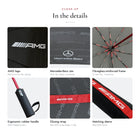 Close-up of the Mercedes-AMG umbrella: AMG logo and Mercedes-Benz star on the canopy, red ribs, rubber handle and AMG sleeve