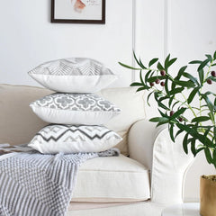 Three grey and white embroidered cushion covers from the set of 4 stacked on a sofa arm beside an olive branch