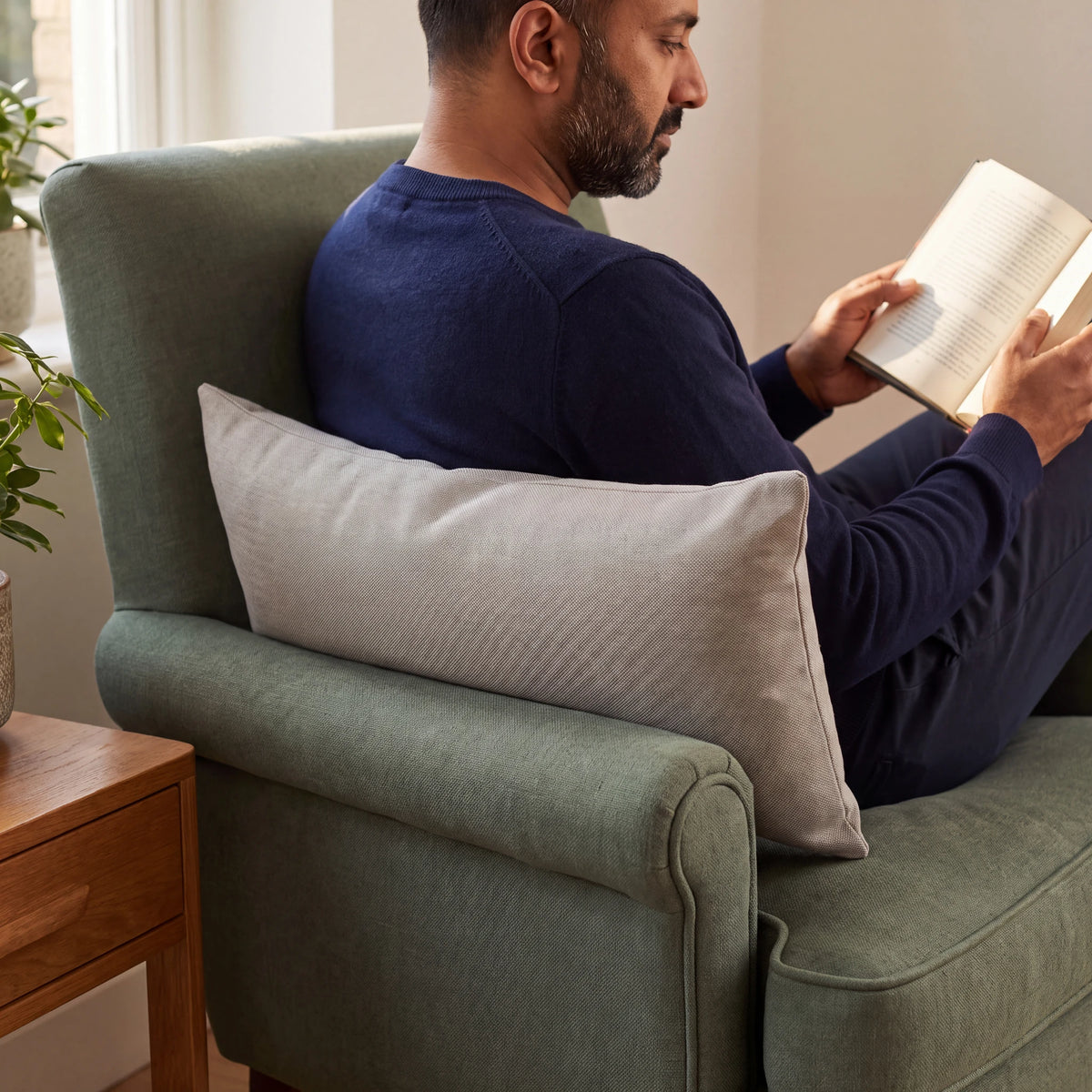 Beige lumbar cushion supporting the lower back of a man reading in a green armchair
