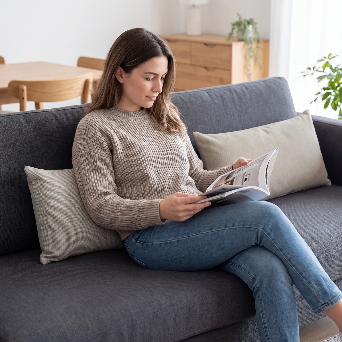 Two neutral beige lumbar cushions on a dark grey sofa with a woman reading a magazine