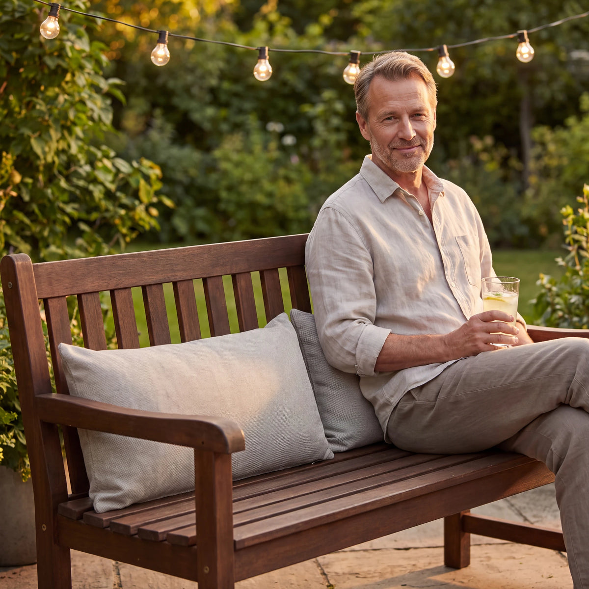Beige outdoor lumbar cushions on a wooden garden bench on a summer evening