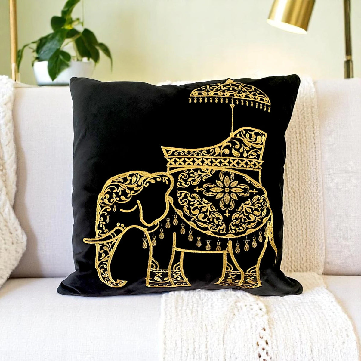 Gold embroidered elephant cushion cover in black velvet on a cream sofa with a knitted throw